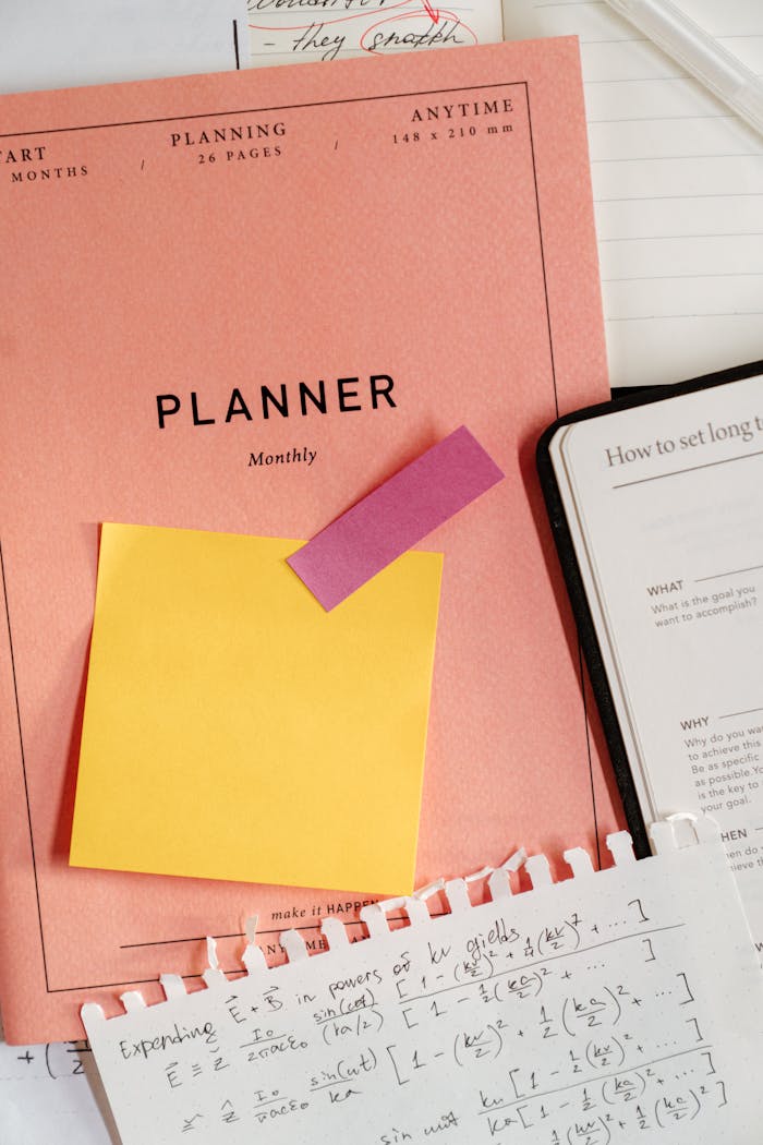 A monthly planner with sticky notes, equations, and a notebook on a desk.